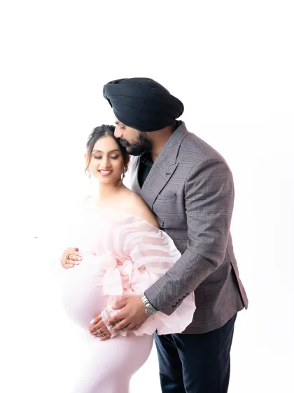 A sweet and gentle moment. The father-to-be kisses his partner's forehead in this light and airy portrait, both dressed in soft, elegant attire.