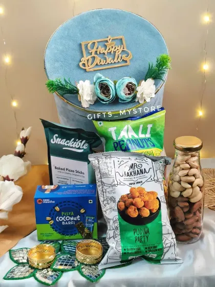This stunning light blue velvet box is filled with a healthy and delicious assortment of snacks. It contains baked pizza sticks, pista-coconut barfi, flavored peanuts, makhana, and a bottle of almonds, along with two decorative diyas.