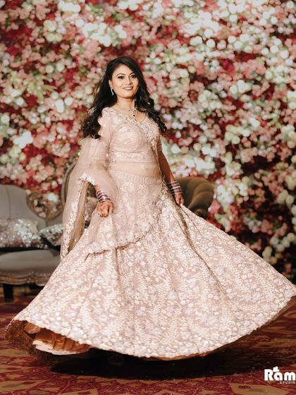 A joyful shot of the bride twirling in her beautiful pastel lehenga against a wall of flowers, capturing her happiness and the beauty of her outfit.