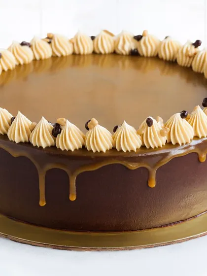 The Chloe cake, our signature blend of chocolate and caramel. This version features a rich chocolate coating, a caramel drip, and a crown of coffee-flavoured buttercream swirls, each topped with a chocolate chip.