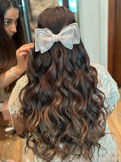 A sweet and beautiful hairstyle for a baby shower, featuring soft waves and a large, elegant bow.