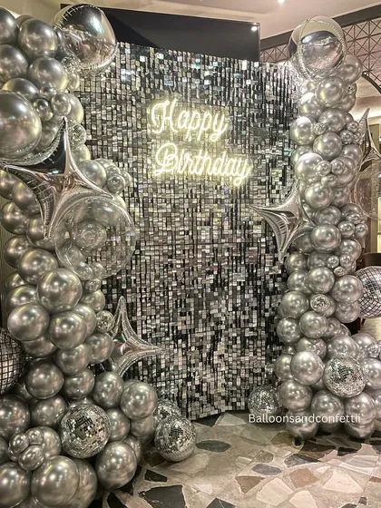 For a birthday that needs to be extra, I designed this full glam setup. It features a silver shimmer wall that catches the light perfectly, framed by an organic arch of chrome and silver balloons, disco balls, and a custom "Happy Birthday" neon sign. This is how you make a statement.