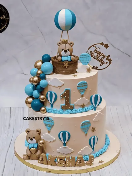A sky-high teddy celebration for a first birthday. This 3kg black forest cake features a teddy in a hot air balloon, surrounded by blue and gold decorative balls and fondant clouds.