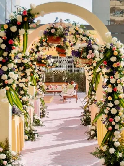 A beautiful floral archway entrance for an urban Haldi. The pastel arches are covered in lush arrangements of white, purple, and peach flowers, creating a soft and romantic welcome.