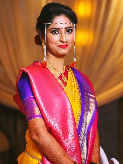 A stunning portrait of a bride in her yellow and pink nine-yard saree, complete with all the traditional Maharashtrian bridal accessories.