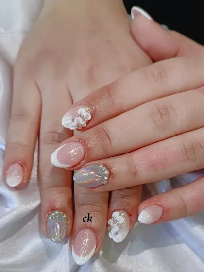 A close-up of a nude bridal set with various textures, including a French ombré, holographic glitter, and 3D flowers with gold bead centers.