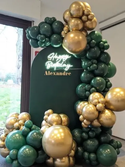 A close-up of the luxurious dark green and gold balloon decor. The quality of the chrome balloons gives this setup a very rich and opulent feel.