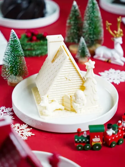 A beautiful white chocolate house, part of a festive Christmas display. The simple, clean styling on a red background makes this intricate creation the star of the show.