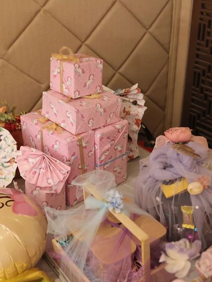 A glimpse of the variety in baby shower gifting. This setup includes unicorn themed wrapped boxes, a baby face balloon, and a beautifully decorated trousseau, creating a stunning gift display.