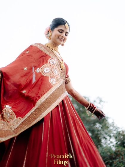 The bride's joyful twirl, her red lehenga flowing around her. A candid portrait that captures her happiness and the beauty of the outdoors.