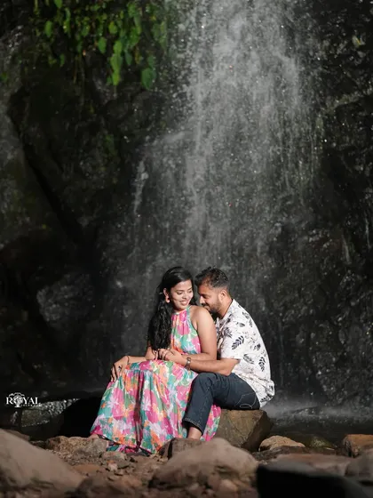 A quiet, romantic shot of a couple sitting on a rock in front of a waterfall, lost in their own world.