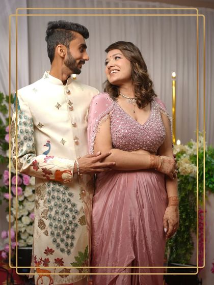 A happy, smiling couple in their unique coordinated outfits. His peacock sherwani and her pink gown are a perfect match.
