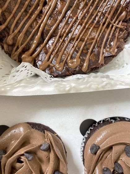 A close-up shot showing the rich frosting on our chocolate cupcakes and the glossy drizzle on the accompanying brownie.