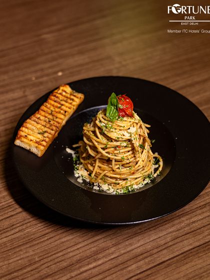 A perfectly twirled spaghetti aglio e olio, garnished with fresh basil and cherry tomato, served with a side of grilled garlic bread. A classic Italian favorite from our Zodiac menu.