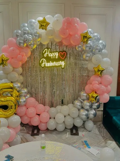 A beautiful circular balloon arch in pink, white, and silver for a 25th anniversary, with a 'Happy Anniversary' neon sign.