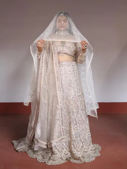 A classic bridal pose with the dupatta used as a veil, showcasing the sheer fabric and delicate border of the pastel lehenga set.