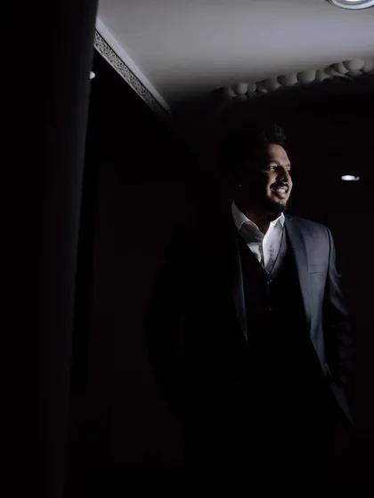 A candid and stylish shot of the groom, captured in a moment of relaxation. The low-key lighting creates a moody and sophisticated portrait.