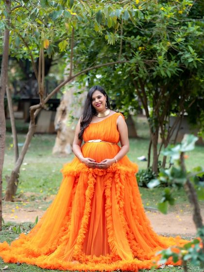 A radiant mom-to-be smiling in a lush green park. Her bright orange ruffled gown looks absolutely stunning against the natural backdrop.