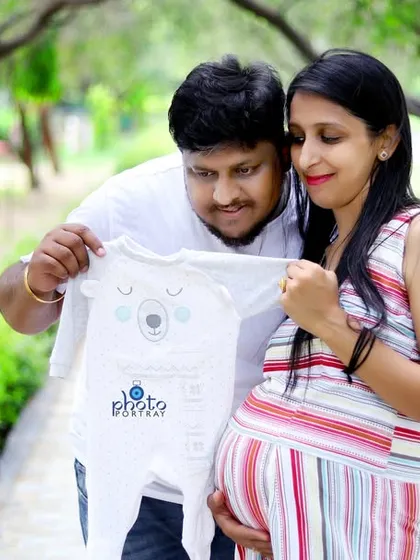 An expecting couple shares a quiet moment in a park, looking at a baby onesie together. This image from an outdoor maternity photoshoot in Noida captures the sweet anticipation of welcoming a new family member.