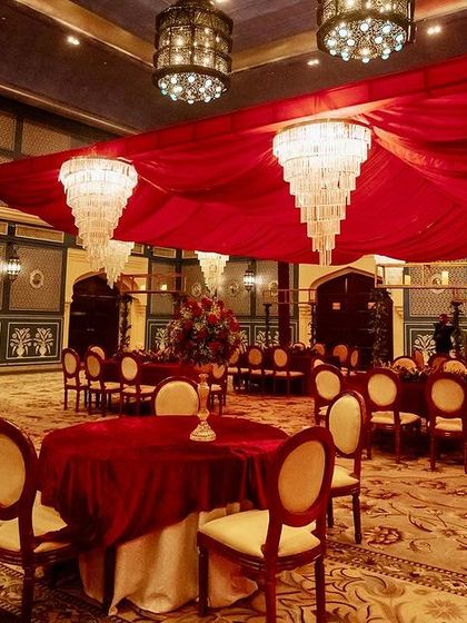 The indoor ballroom transformed for a royal wedding, with a ceiling of red drapes and crystal chandeliers complementing the venue's regal architecture.