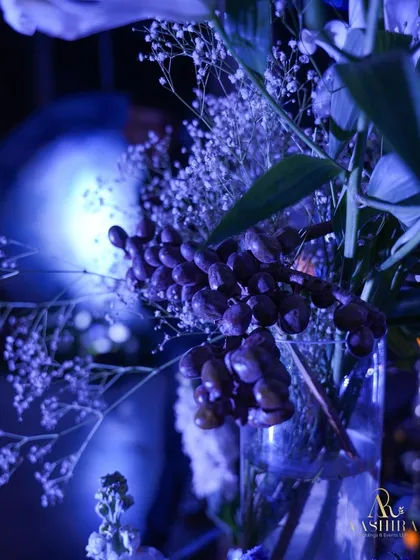 A macro shot of the floral decor, showing a bunch of grapes integrated into the arrangement against the soft blue, out-of-focus background.