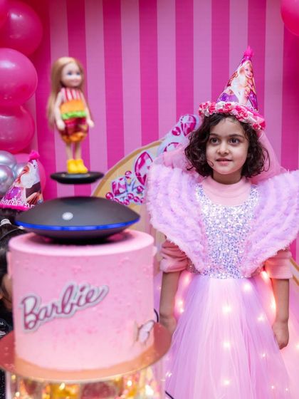 The birthday girl, dressed in a light-up angel Barbie costume, stands beside her equally magical rotating Barbie cake.
