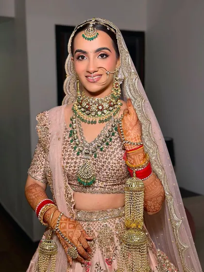 A smiling bride looking radiant in her pastel pink Dolly J Studio lehenga. Her makeup is flawless and fresh, perfect for a modern wedding celebration.