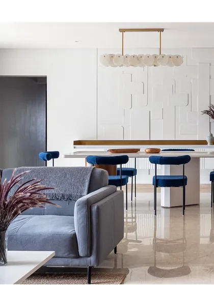 A full view of the stunning dining area in 'Vishu Home'. The monolithic white table and bold blue chairs are the centerpiece, set against a custom-designed textured wall that adds depth and interest.