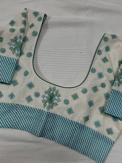 This white and green cotton blouse features a beautiful combination of geometric and floral Kasuti patterns. It's a fresh and elegant design, perfect for summer.