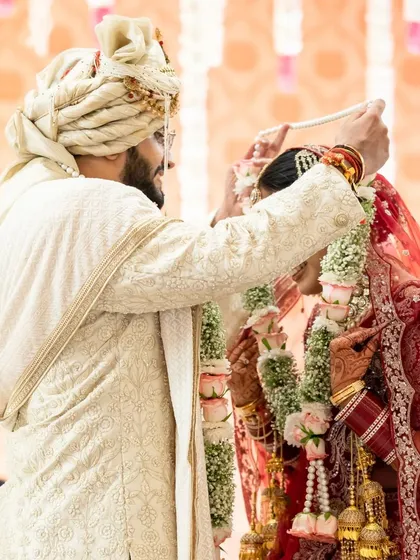 The groom places the garland on the bride, a moment of acceptance and love. The focus is on the ritual and their gentle expressions.