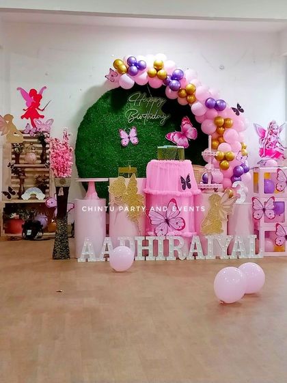 A butterfly and fairy themed birthday party in pink and purple. This elaborate setup includes a faux grass wall, a balloon arch, and multiple dessert tables with fairy-themed props.