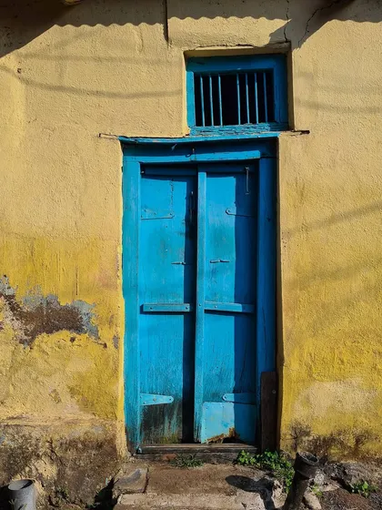 A vibrant blue door provides a striking contrast against a weathered yellow wall. This simple yet powerful composition highlights the bold use of color in traditional Indian village architecture.