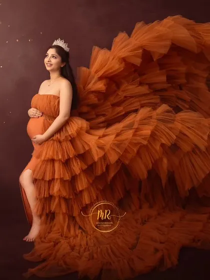 A powerful side-profile shot in a dramatic orange gown. The fabric is tossed to create a stunning visual effect, highlighting the mother's silhouette against a starry backdrop.
