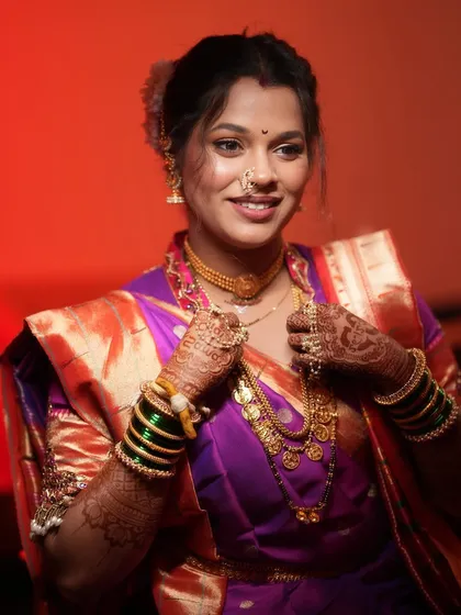 This Maharashtrian bride looks radiant, adjusting her traditional gold jewelry. The makeup is focused on a natural glow that complements her intricate henna and wedding attire.