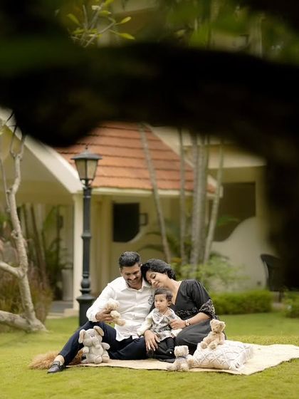 A family of three enjoys a picnic on a lush green lawn, with their beautiful home visible in the background.