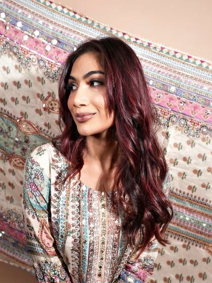 The ruby-toned hair styled in loose waves, perfectly complementing the client's traditional attire. This shows how a modern hair colour can beautifully pair with ethnic wear.