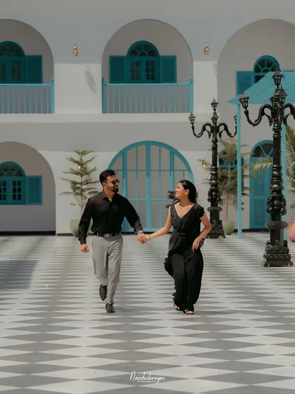 A joyful, dynamic shot of a couple running hand-in-hand through a courtyard with a distinctive black-and-white checkered floor.