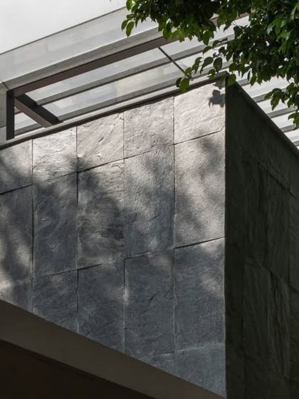 The exterior facade features locally sourced slate stone cladding. This detail shot highlights the texture and durability of the material, grounding the modern structure in its local context.