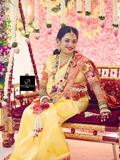 The complete look for a traditional baby shower. The mom-to-be is seated on a decorated swing, wearing a handcrafted floral set with a necklace, kamarbandh, and hand pieces.