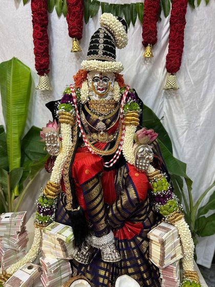 A grand and opulent pooja setup, with the Goddess draped in a rich red and black checked silk saree, surrounded by offerings of wealth.