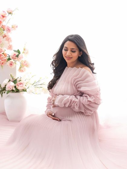 A quiet, contemplative moment. Seated amongst soft pink florals, the mom-to-be gently cradles her bump in this serene and beautiful portrait.