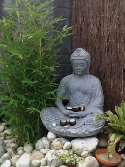 A meditative space created with a sitting Buddha statue, young bamboo plants, and a bed of smooth white river stones. The natural textures create a simple yet elegant design.