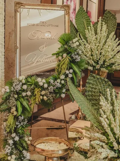 A personalized welcome mirror in a vintage gold frame, adorned with lush white and green floral arrangements.