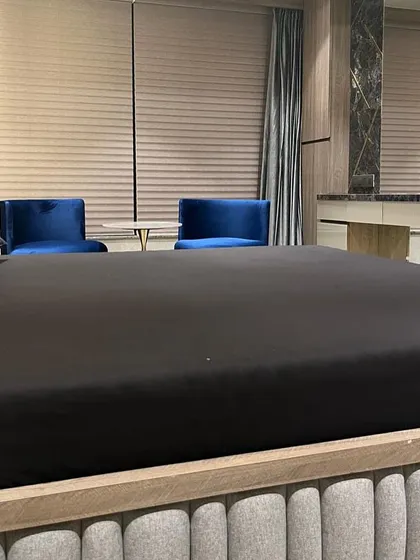Another perspective of the Juhu residence bedroom, showing how a large, simple circular mirror can act as a statement piece. The dark bedding and rich blue chairs add a touch of drama and depth to the space.