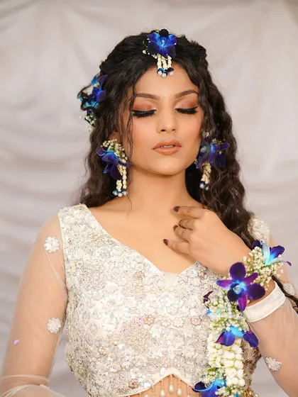 Whites and blooms, a perfect blend. This look features a white lehenga adorned with fresh blue and white floral jewelry, perfect for a Haldi or Mehendi.
