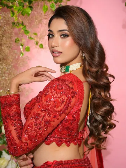 A beautiful profile shot showcasing the soft curls and radiant makeup on the sister of the groom, highlighting the intricate details of her red lehenga.