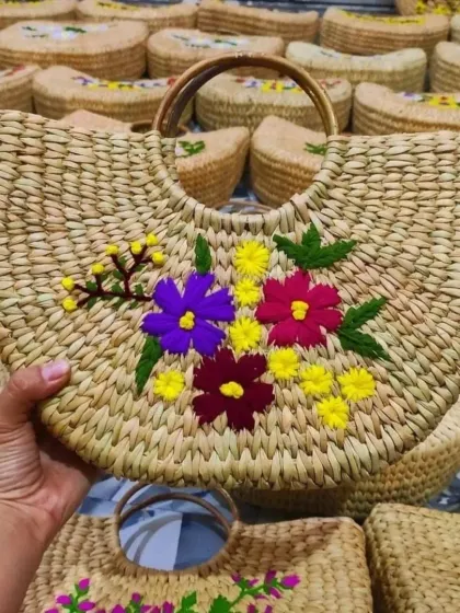 A hand holds up one of our beautifully embroidered bags, with many more in the background. This demonstrates the product in hand and also our capacity for bulk production, perfect for wholesale inquiries.