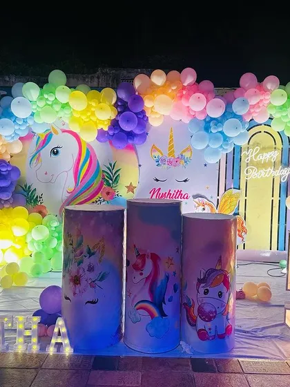 A magical unicorn theme for a 5th birthday. This decoration features a unicorn and rainbow backdrop, a colorful balloon arch, themed plinths, and a large marquee number '5'.