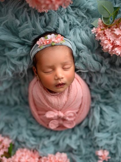 Learning to combine colors effectively can make your images pop. The contrast between the soft pink wrap and the textured teal backdrop, framed by flowers, creates a visually stunning portrait.