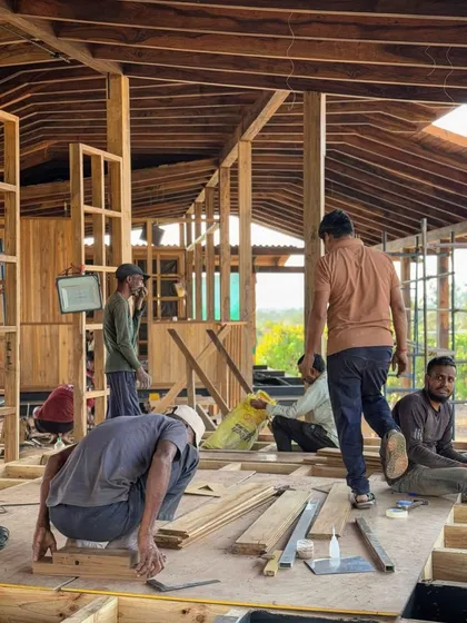 Carpenters work on the wooden flooring and framing inside the farmhouse. The entire interior is a celebration of timber construction, with every piece cut and joined by hand.